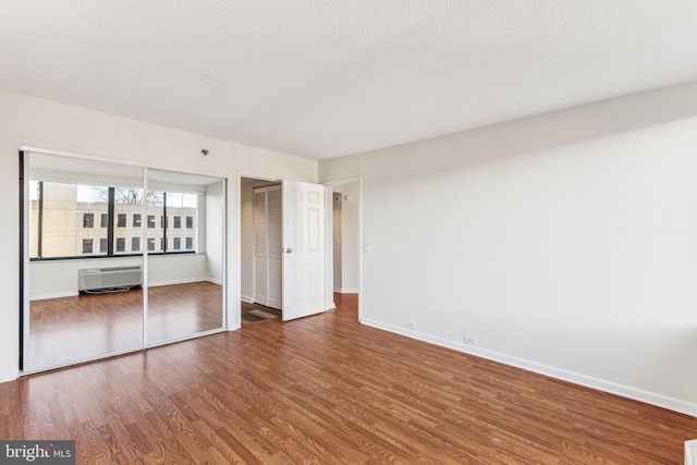 unfurnished bedroom with a textured ceiling, wood finished floors, and baseboards