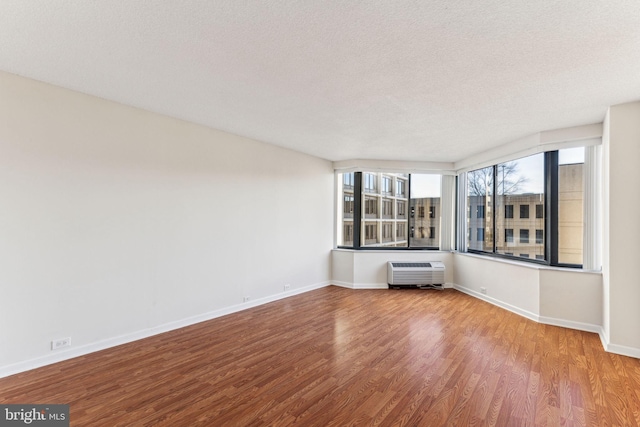 unfurnished room featuring a textured ceiling, a wall mounted AC, baseboards, and wood finished floors