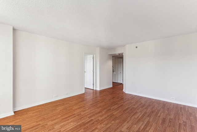 spare room featuring a textured ceiling, wood finished floors, and baseboards