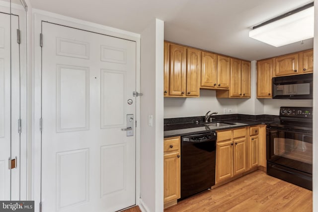 kitchen featuring light wood-type flooring, black appliances, dark stone counters, and a sink