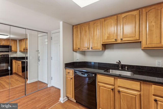 kitchen with light wood-style floors, dark stone counters, a sink, and black appliances