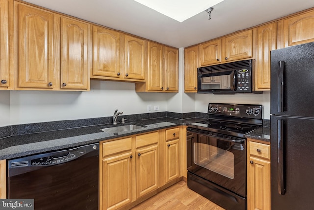 kitchen with dark stone countertops, a sink, light wood finished floors, and black appliances