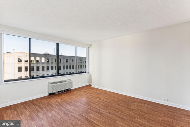 empty room featuring a textured ceiling, a wall unit AC, wood finished floors, and baseboards