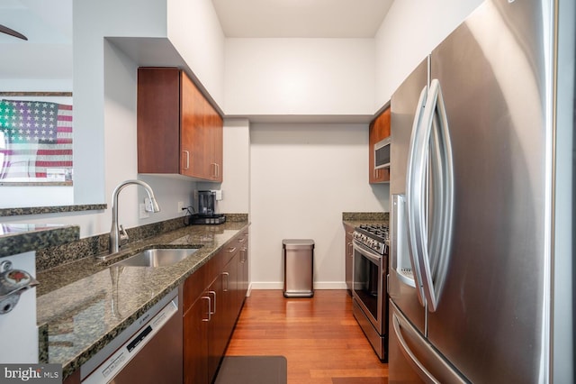 kitchen with light wood finished floors, dark stone countertops, appliances with stainless steel finishes, and a sink