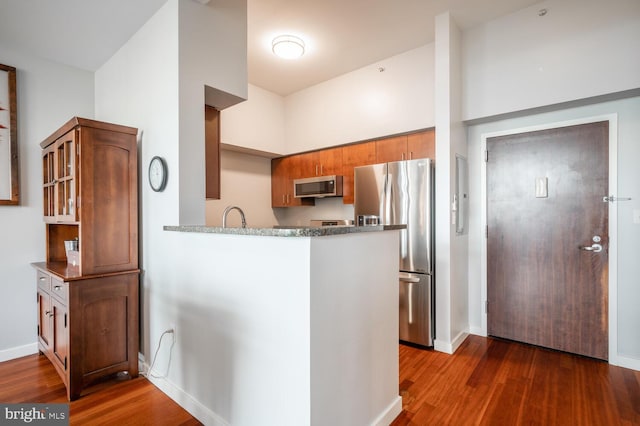 kitchen with dark wood-style flooring, appliances with stainless steel finishes, brown cabinetry, glass insert cabinets, and baseboards