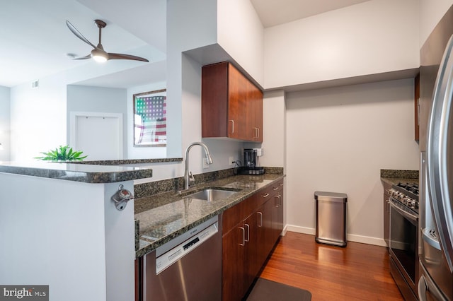 kitchen with dark wood finished floors, a ceiling fan, dark stone countertops, stainless steel appliances, and a sink