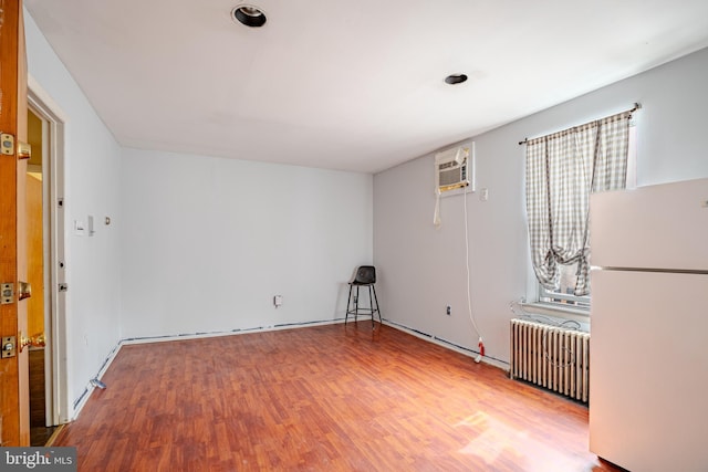 empty room with a wall mounted air conditioner, wood finished floors, and radiator