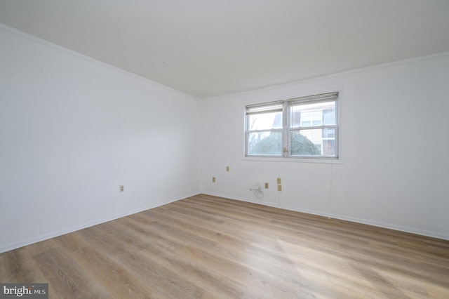 empty room with ornamental molding, light wood-style flooring, and baseboards