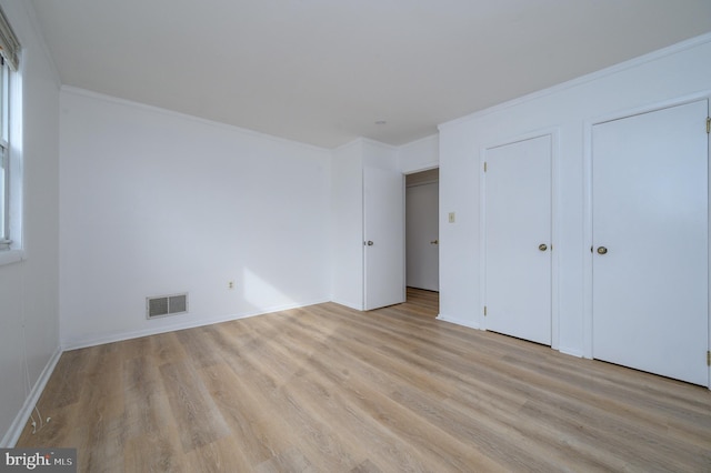 unfurnished bedroom featuring light wood finished floors, baseboards, visible vents, and ornamental molding