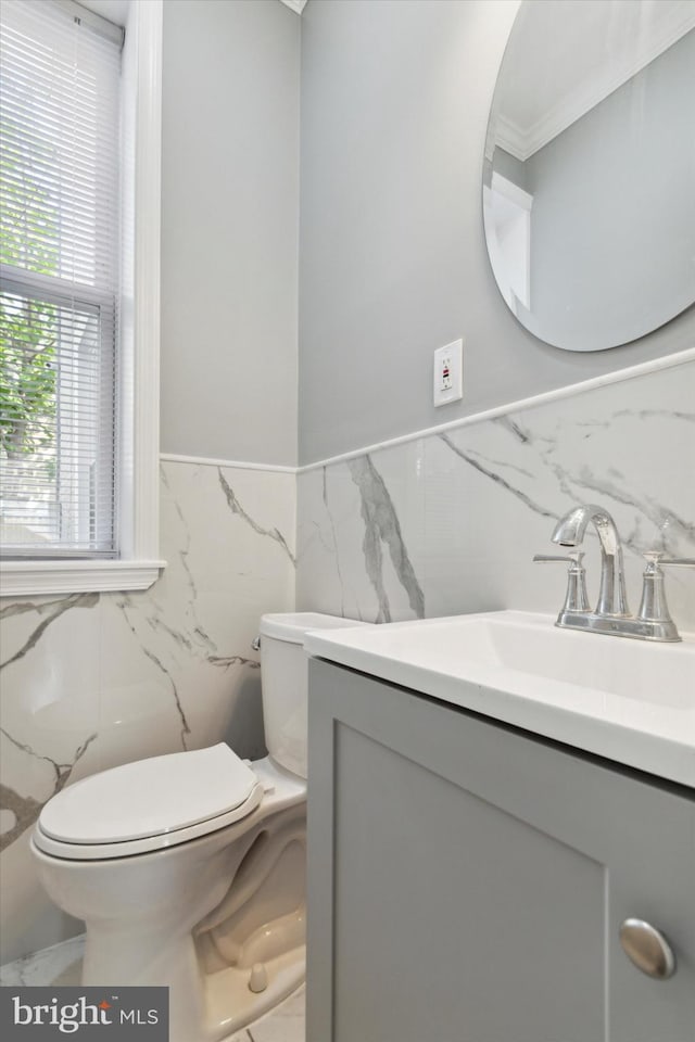 bathroom featuring toilet, a wainscoted wall, marble finish floor, vanity, and tile walls