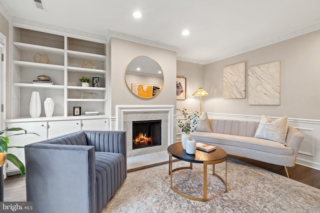 living area featuring a premium fireplace, wood finished floors, visible vents, built in features, and crown molding