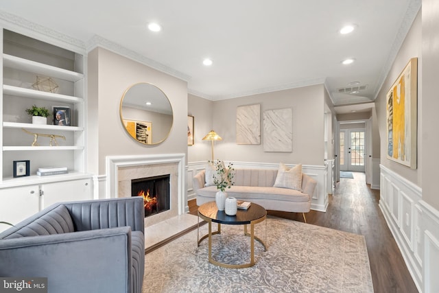 living area with visible vents, a wainscoted wall, a premium fireplace, dark wood-type flooring, and built in shelves