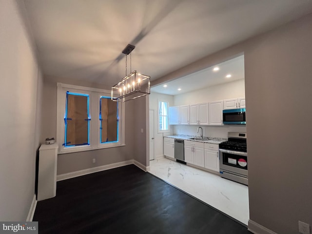 kitchen featuring pendant lighting, stainless steel appliances, white cabinets, a sink, and baseboards