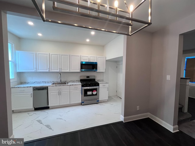 kitchen featuring baseboards, white cabinets, appliances with stainless steel finishes, light stone countertops, and a sink