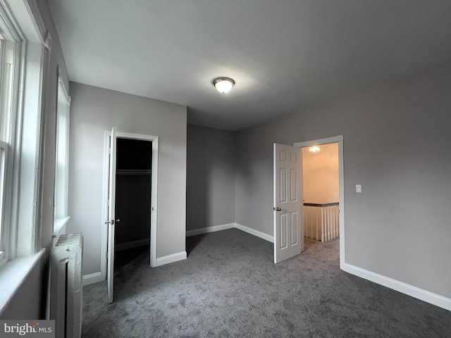 unfurnished bedroom featuring radiator, baseboards, and dark carpet