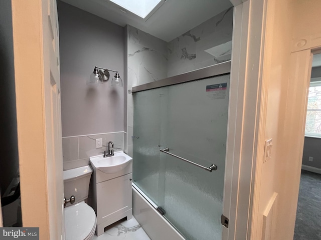 full bath with a skylight, marble finish floor, bath / shower combo with glass door, toilet, and vanity