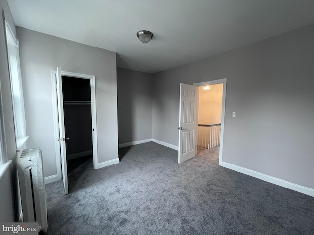 unfurnished bedroom with a closet, baseboards, dark carpet, and radiator heating unit