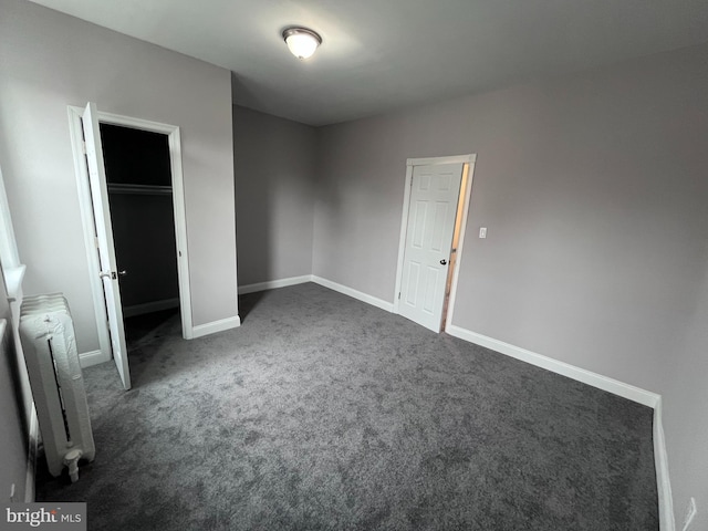 unfurnished bedroom with a closet, radiator, dark carpet, and baseboards