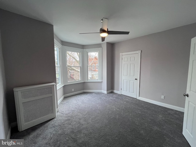 unfurnished bedroom featuring a ceiling fan, dark colored carpet, heating unit, and baseboards