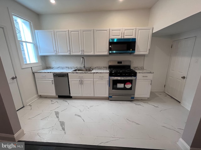 kitchen featuring stainless steel appliances, a sink, white cabinets, marble finish floor, and light stone countertops