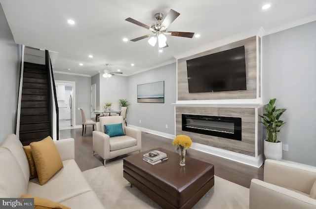 living room featuring a glass covered fireplace, crown molding, light wood finished floors, and recessed lighting