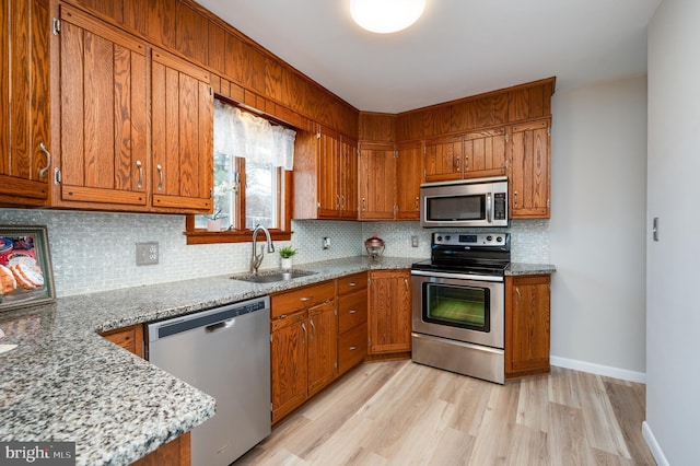 kitchen with light stone counters, stainless steel appliances, decorative backsplash, brown cabinetry, and a sink