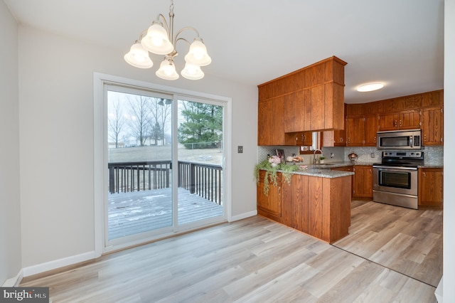 kitchen with brown cabinets, stainless steel appliances, hanging light fixtures, backsplash, and a peninsula