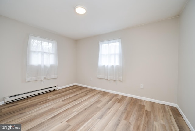 spare room featuring a baseboard heating unit, light wood-style flooring, and baseboards