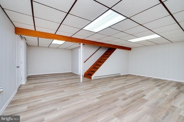 finished basement with stairs, baseboard heating, light wood-type flooring, and a paneled ceiling