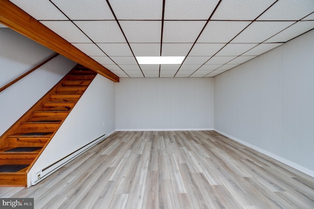 finished basement with a baseboard heating unit, a drop ceiling, light wood-style flooring, and baseboards