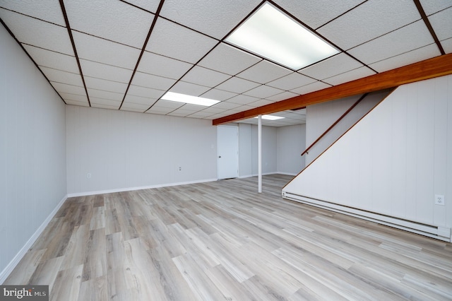 finished below grade area featuring a paneled ceiling, light wood finished floors, baseboards, and baseboard heating