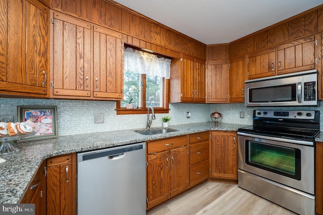 kitchen featuring light stone counters, appliances with stainless steel finishes, brown cabinetry, and a sink