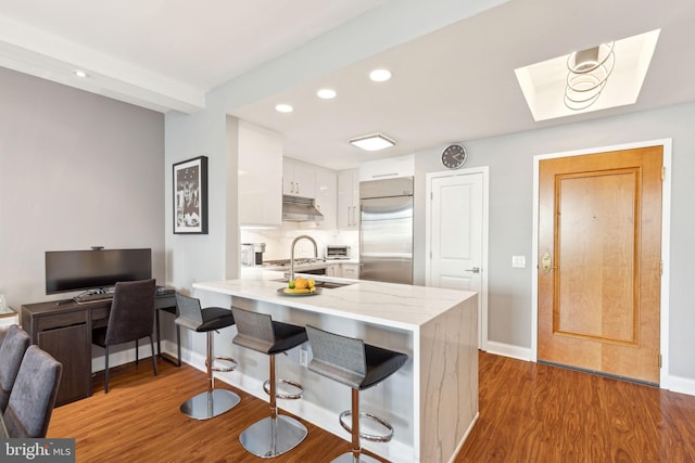 kitchen with a breakfast bar, white cabinets, stainless steel built in fridge, wood finished floors, and a peninsula