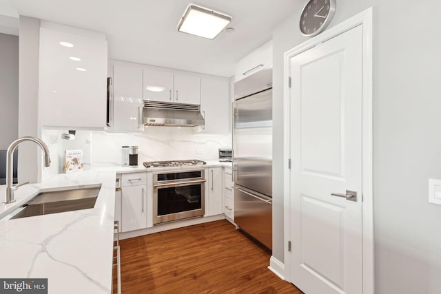 kitchen featuring tasteful backsplash, appliances with stainless steel finishes, under cabinet range hood, white cabinetry, and a sink