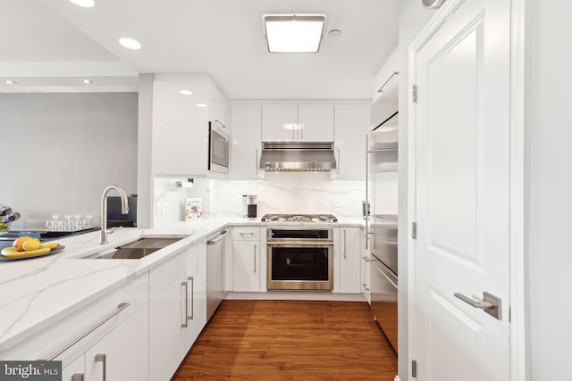 kitchen with decorative backsplash, white cabinets, built in appliances, a sink, and exhaust hood