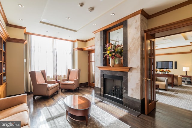 sitting room with wood-type flooring, a fireplace, a raised ceiling, and crown molding