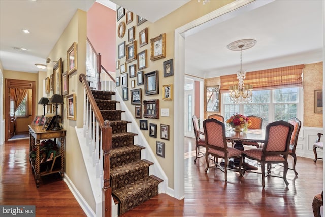 dining area featuring stairs, dark wood-type flooring, a wainscoted wall, and a chandelier