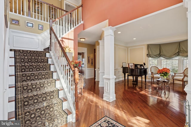 stairs with decorative columns, ornamental molding, wood finished floors, a high ceiling, and a decorative wall