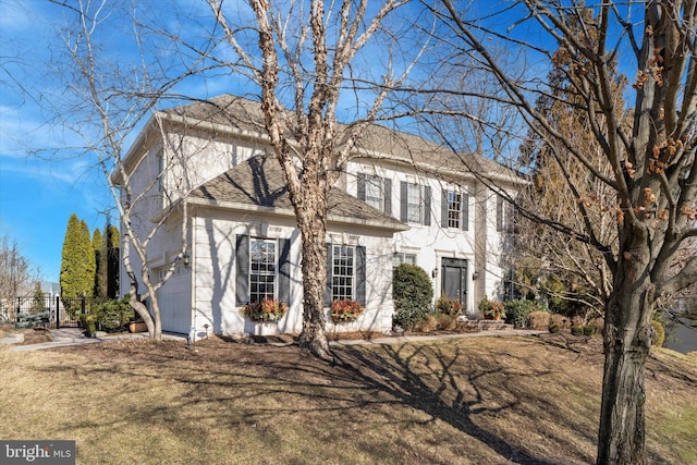 colonial home featuring an attached garage, roof with shingles, and a front yard