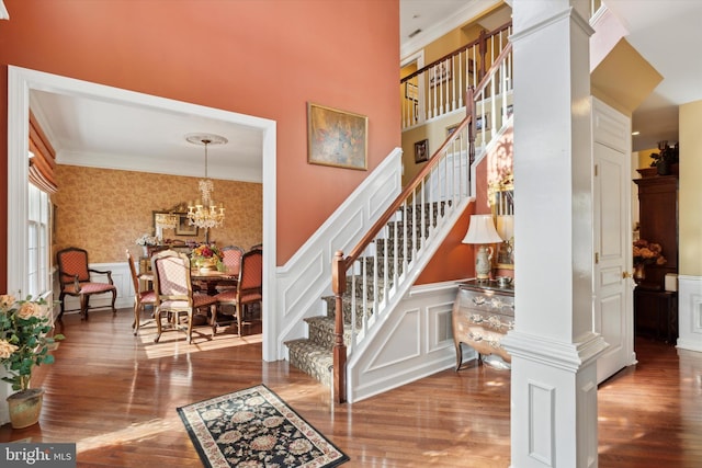 staircase with ornamental molding, a decorative wall, ornate columns, and wood finished floors