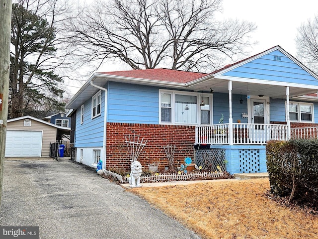 view of front of home with aphalt driveway, an outbuilding, brick siding, a detached garage, and covered porch