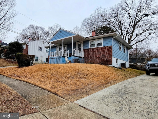 view of front of property featuring covered porch, brick siding, and a chimney