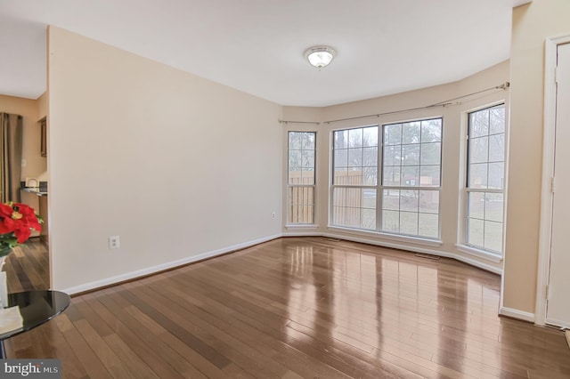 unfurnished room with baseboards, visible vents, and wood finished floors