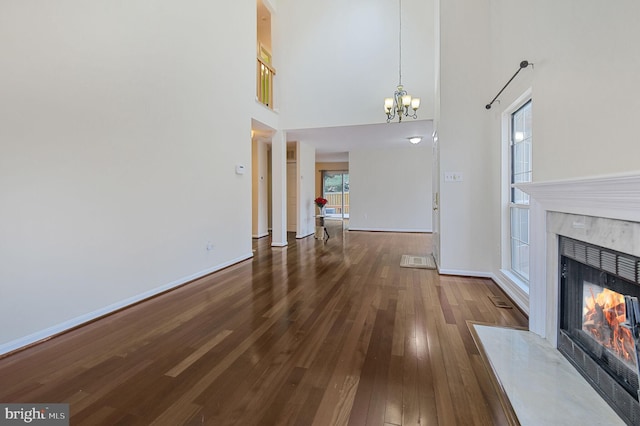 unfurnished living room with a fireplace, a towering ceiling, wood finished floors, a chandelier, and baseboards