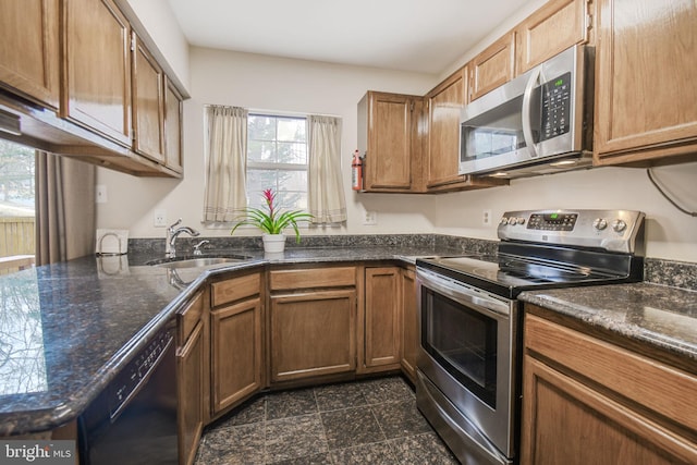 kitchen with appliances with stainless steel finishes, brown cabinetry, a sink, and granite finish floor