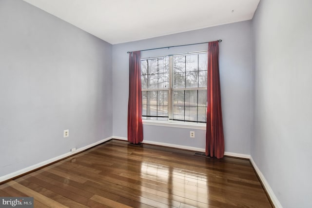 empty room with dark wood-style floors, visible vents, and baseboards