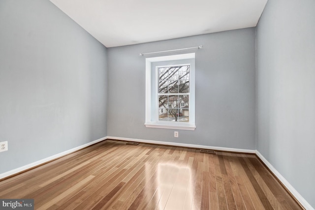 unfurnished room featuring wood finished floors, visible vents, and baseboards