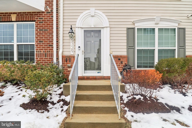 snow covered property entrance featuring brick siding