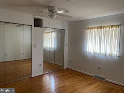 unfurnished bedroom with baseboards, light wood-style flooring, visible vents, and multiple closets