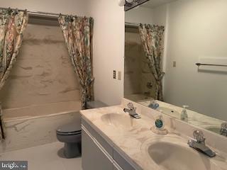 full bathroom with double vanity, a sink, toilet, and shower / tub combo with curtain